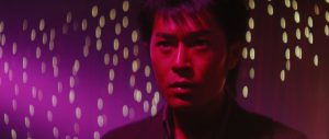 Un homme en rapproché-épaule, dans ce que l'on devine être une boîte de nuit, devant un mur violet tachées par des lueurs dorées, plan du film Judo.