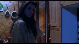 Une jeune femme brune, l'air songeur, dans une cuisine plongée dans une lumière bleutée dans le film Le couteau sous la gorge.