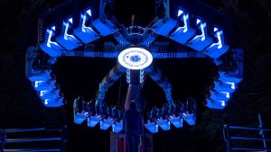 Le personnage de Zumbo est face à une attraction de fête foraine, dans la nuit, éclairée d'un bleu surréaliste ; la femme paraît toute petite face à la machine.