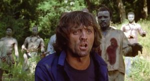 Dans ce qui semble être une jungle, un homme tente d'échapper à un groupe de zombies qui marche vers lui ; scène du film Virus Cannibale.