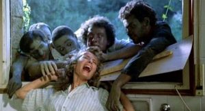 Cinq zombies, passant leurs bras par une large fenêtre, tirent une femme apeurée par les cheveux dans le film Virus Cannibale.