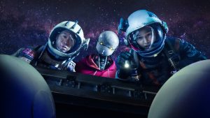 Deux astronautes, un homme et une femme se penchent sur une machine, intrigués ; entre eux se trouve un robot ; derrière eux, un ciel intersidéral violet ; scène du film Space sweepers.