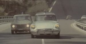 Sur une autoroute de Gênes, une voiture de police poursuit une ambulance ; scène du film Le Témoin à abattre.