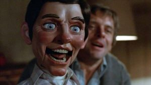 Au premier plan, une marionnette masculine avec un sourire inquiétant, au second plan Anthony Hopkins qui l'actionne l'air hagard ; scène du film Magic.