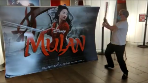 Un homme s'apprête à détruire un PLV du film Mulan, blockbuster 2020,avec une batte de base-ball.