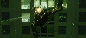 Trinity, dans Matrix, vient de traverser une fenêtre et tire dans l'air avec ses deux revolvers.