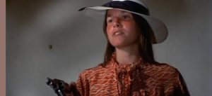 Barbara Hershley brandit son revolver d'un air absent, sous un joli chapeau féminin, scène du film Bertha Boxcar.