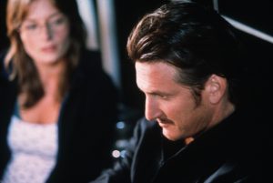 Au premier plan, Sean Penn pensif, en rapproché-épaule, vu de profil ; au second plan, flou, une jeune femme le regarde ; plan du film Le Poids de l'Eau.