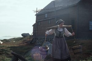 Près d'une maison au bord de la mer, une femme vêtue comme un paysanne d'un ancien temps porte sur ses épaules deux seaux dans le film Le Poids de l'Eau.