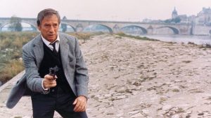 Sur les rives de la Loire, un pont d'Orléans en arrière-plan, Yves Montand dégaine son revolver, prêt à tirer dans le film Police Python 357.