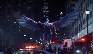 Ce qui semble être un ange géant, aux ailes déployées, tient une femme dans ses bras au beau milieu d'une rue remplie remplie d'ambulances et de voitures de police ; scène de la série Falcon et le soldat de l'hiver.