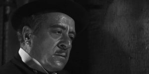 Gros plan sur le visage de Raimu, fermé, en sueur, portant un chapeau noir dans le film L'étrange Monsieur Victor.