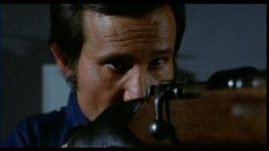 Gros plan sur Henry Silva l'oeil dans le viseur de son fusil dans le film Le boss, issu de la Trilogie du Milieu.