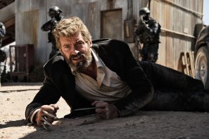 Hugh jackman à terre sur le sable, tenu en joug par trois membres du SWAT dans le film Logan.