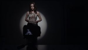Amanda Fuller passe un casting dans une pièce dans la pénombre ; devant la caméra, elle est éclairée par un seul projecteur circulaire ; scène du film Starry Eyes.