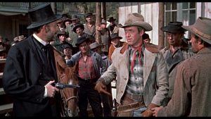 Dans une rue bondée de badauds, James Stewart est tenu sous le revolver du marshall tout vêtu de noir dans le film Je suis un aventurier.