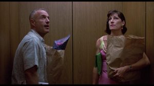 Un homme et une femme qui semble-t-il ne se connaissent pas sont dans un ascenseur, un sac de course en papier dans les bras ; leur regard est dirigé vers le haut de la cabine, comme s'ils avaient entendu un bruit ; scène du film Peggy Sue s'est mariée de Francis Ford Coppola.
