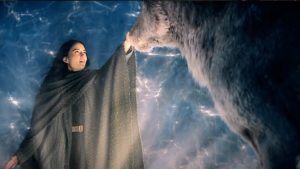 Alina, baignée dans une lumière et un ciel sunaturels, touche le museau d'un loup géant dans la série Shadow and Bone : la saga Grisha.