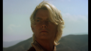 Plan rapproché-épaule sur le blond et jeune Sebastian Harrison interprétant Shining Sky, au coeur des montagnes, regardant l'horizon dans le film Bianco Apache.