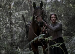 Clara marche à côté de son cheval dans la forêt dans le film The Nightingale.