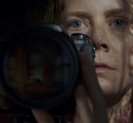 Gros plan sur le visage d'Amy Adams les cheveux mouillés, derrière un appareil photographique ; son regard n'est pas dirigé vers l'écran de contrôle de l'appareil mais vers l'horizon ; plan issu du film La Femme à la Fenêtre.