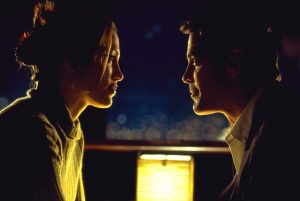 George Clooney et Jennifer Lopez attablés, face à face, au dessus d'une petite lampe jaune qui diffuse un beau clair-obscur ; plan issu du film Hors d'atteinte.