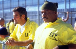 Ving Rhames et George Clooney en tenue de prisonniers jaunes observent la cour de la promenade de la prison dans le film Hors d'atteinte.