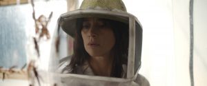 Plan rapproché-épaule sur l'actrice Suliane Brahim portant un casque de protection contre les insectes volants et observant son élevage de sauterelles dans le film la Nuée de Just Philippot.