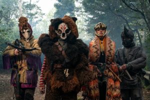 Quatre individus posent avec des armes ; ils portent des masques d'animaux ou de squelettes et des tenues inspirées par la fourrure et d'autres peaux animales ; personnages issus de la série Sweet Tooth. 