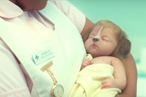 Un nourrisson humain à museau d'animal dort dans les bras d'une infirmière dans la série Sweet Tooth.