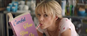 Carey Mulligan lit un livre dans une boutique, une paille dans la bouche, l'air enfantin dans le film Promising Young Woman.