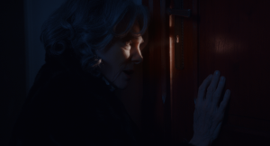 Jacqueline Bisset regarde à travers la serrure d'une porte, dans un plan au fort clair-obscur de Messe Basse réalisé par Baptiste Drapeau.