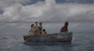 Cinq enfants se tiennent dans une barque vétuste, au milieu de l'océan sous un ciel nuageux dans le film Wendy.
