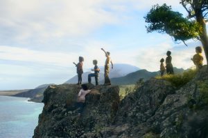 Des enfants debout au bord d'une falaise, dans un magnifique paysage de bord de mer montagneux ; scène du film Wendy.
