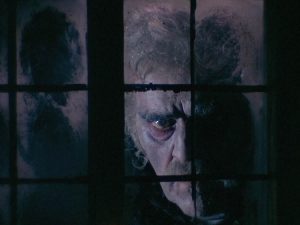 Un vieil homme au teint pâle et aux traits cadavériques regardent d'un air sombre à travers une fenêtre sale, scène de nuit du film Les Wurdulaks de Mario Bava.