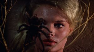 Gros plan sur le visage d'une jeune femme blonde, les yeux rivés sur une grosse araignée au premier plan ; plan issu du film Les trois visages de la peur de Mario Bava.