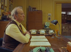 Bill Murray s'ennuie assis à son bureau, les bras croisés, dans le film The French Dispatch.