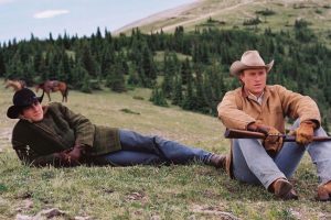 Jake Gyllenhal et Heath Ledger sont côté à côté sur un flanc de vallée, vêtus en cow-boy, ils observent l'horizon dans le film Le secret de Brokeback Mountain de Ang Lee.