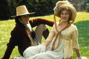 Greg Wise et Kate Winslet sont assis sur l'herbe sous le soleil, vêtu comme au 19ème siècle, tout sourire dans le film Raison et sentiments de Ang Lee.