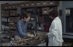 Jeanne Balibar, portant une veste de scientifique, et Tilda Swinton, observent un squelette fossile, dans une bibliothèque ; scène du film Memoria.