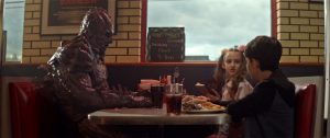 Mimi, Luke et le monstre Psycho Goreman, mi-homme mi-poisson-lézard, mangent tranquillement à la table d'un dinner dans le Psycho Goreman.