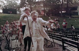 On expulse un vieillard en cannes d'une représentation en plein air ; le viel homme est poussé en hurlant entre de nombreux bancs vides dans le film The Amusement Park.
