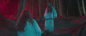 Dans une forêt étrange baignée dans une lumière rouge et bleue turquoise, deux filles aux cheveux longs, en robe blanche, se font face ; l'une d'entre elles tient une hache, nous voyons l'autre de dos ; plan issu du film Censor.