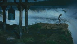 Plan large du film L'étang du démon sur un véritable déluge et une falaise déchaînée ; au bord de l'image à droite, un homme esseulé contemple les torrents.