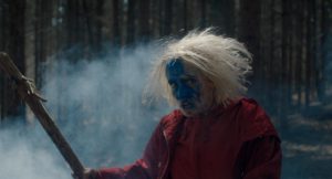 Dans la forêt, Eve, le visage peint en bleu, tient un bout de bois qu'elle tient avec un air de guerrière dans le film Hunted.