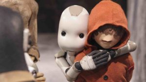 Face à un miroir, un petit robot blanc enlace ce qui a l'air d'être un petit garçon, avec une bouche qui ressemble à un bec, le haut du visage caché par une capuche rouge ; plan issu du film Junk Head.