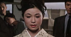 Plan rapproché-épaule sur une jeune femme en kimono, le regard en bas, l'air perdu ; derrière elle, un couple et un homme en costume-cravate la regardent ; scène du film La bête élagante.