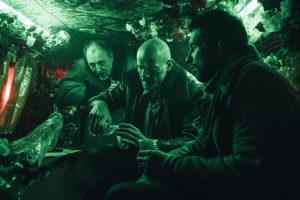 A l'arrière d'un van en bazar baigné dans une lumière verte, trois hommes boivent un verre, tous l'air de bandits dans le film La fièvre de Petrov.
