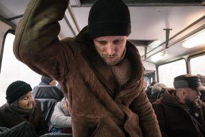 L'acteur Semyon Serzin debout dans un bus, se tient à la rembarde ; il porte un manteau polaire et un bonnet, il semble fatigué et fermé, le regard dirigé vers le sol ; scène du film La fièvre de Petrov.