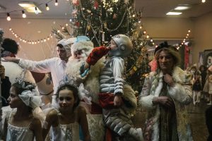 Une fête de Noël dans ce qui semble être un hôpital, beaucoup de monde devant un sapin de Noël, deux petites filles déguisées en danseuses, et un Père Noël qui tient un enfant en costume d'astronaute dans ses bras ; plan issu du film La fièvre de Petrov.
